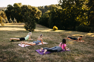 Group of women lying on yoga mats outdoors during relaxation or stretch pose. Mindfulness, recovery, wellness and healthy lifestyle concept.