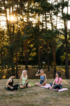 Group of women sitting and talking after outdoor yoga session in a park. Community, friendship, relaxation and wellness lifestyle concept.