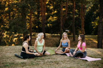 Group of women sitting together and talking after outdoor yoga session in a park. Community, friendship, relaxation and wellness lifestyle concept.