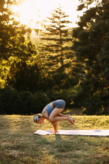 Strong woman practicing crow pose yoga balance outdoors, demonstrating control, focus, and advanced yoga skills in warm evening light.