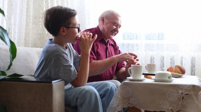 An older man and a boy share breakfast, laughing and playfully high fiving over sandwiches, warm, joyful intergenerational moment at a sunlit table.