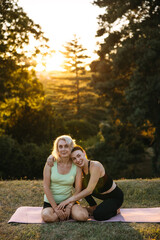 Young woman hugging an older woman after outdoor yoga session at sunset. Mother and daughter or friends bonding, wellness, care, and healthy lifestyle concept.