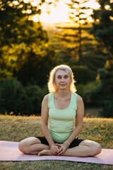 Serene mature woman practicing yoga outdoors at sunset, sitting cross-legged on a mat in a peaceful park, promoting wellness, mindfulness, and healthy aging.