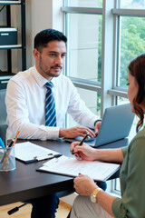 Young man sitting at desk using laptop while listening to adult woman writing on document during business meeting in office