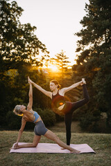 Two women practicing partner yoga pose outdoors at sunset. Balance, teamwork and mindful fitness training in natural environment.