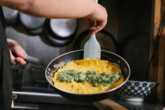 Person cooking omelette with spinach filling in pan