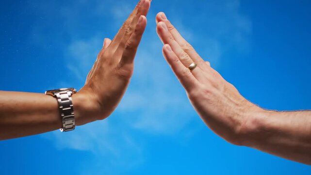 Against a vibrant blue sky, two hands  &mdash;one with a watch, one with a ring  &mdash;clap together, releasing a dramatic cloud of white powder upon contact before quickly separating and exiting the frame.