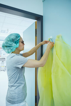 Doctor taking personal protective equipment from hook in hospital