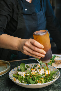 Chef dressing a fresh arugula salad with goat cheese