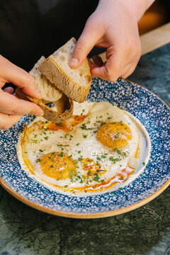 Hands dipping sourdough bread into traditional turkish eggs