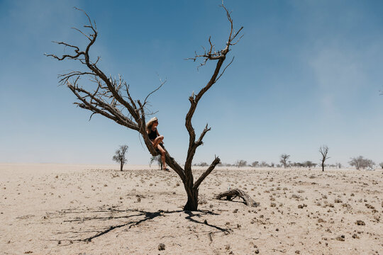 Namibia, Way to Sossusvlei, woman sitting in dead tree in the desert