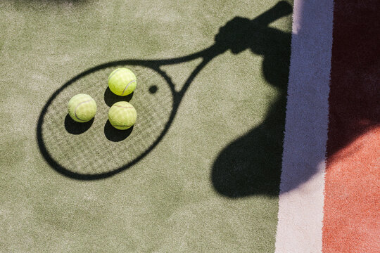 Shadow of a tennis player with balls and racket on court