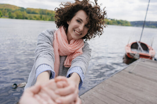Woman standing on jetty, pulling on man's hand