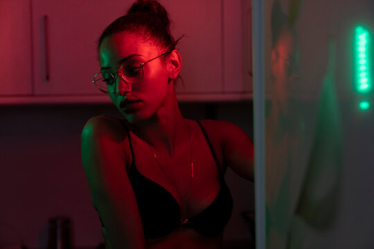 Portrait of beautiful young woman wearing bra and glasses in a dark illuminated room