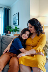 Adult woman sitting on sofa embracing preteen girl who is leaning against her, both showing affectionate expressions in cozy living room setting