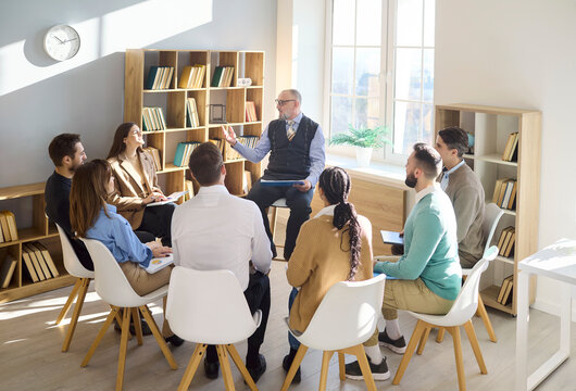 Group students and professor in library seminar. Seated in a circle, they listen and exchange ideas. Ideal for education, coaching and training. Clear mentoring and leadership concept.