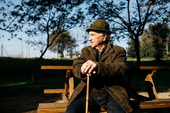 Old man with cane sitting on banch in a park