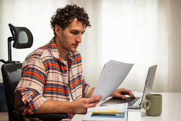 Focused businessman using laptop and examining documents while working from his cozy home.	