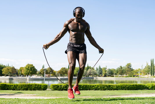 Sportsman doing skipping exercise while listening music through headphones in park on sunny day