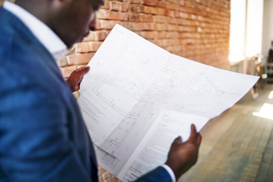 Businessman studying construction plan at brick wall