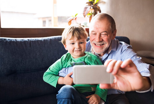 Grandfather and grandson sitting on couch,taking smartphone selfies