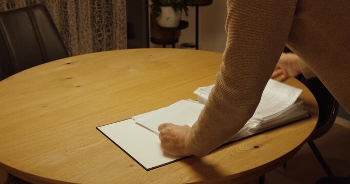 Cinematic stock footage showing hands flipping through documents in a binder on a wooden table, symbolizing document management, information search, administration, and organized office work.