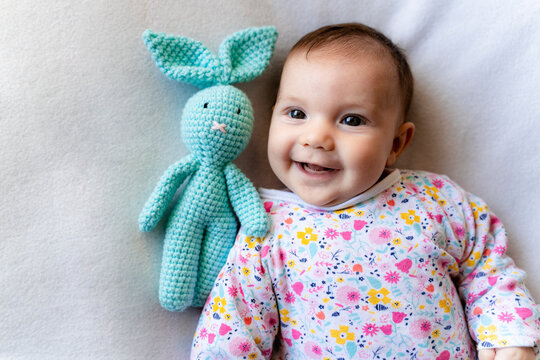Baby girl with a bunny toy lying on bed