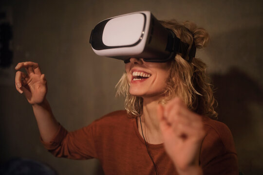 Laughing young woman using Virtual Reality Glasses at home