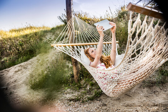Woman lying in hammock taking a selfie with tablet