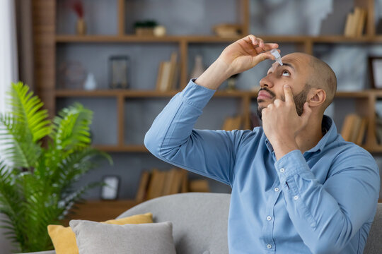 Man applying eye drops from a small medical bottle, treating dry eyes and practicing self-care at home with gentle precision for relief, hydration and everyday eye health