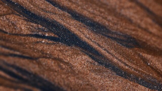 Magical natural patterns formed by black sand on multicolored Hormuz Island beach, Iran. Dark mineral sands including hematite, ilmenite, and magnetite create striking abstract textures 