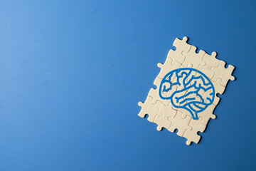 Top view of white jigsaw puzzle with blue human brain drawing on blue background with copy space. Mental health, autism awareness, psychology, and logic problem solving concept.