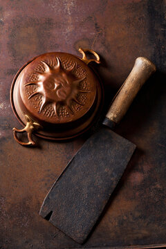 Old copper baking dish and cleaver on rusty ground