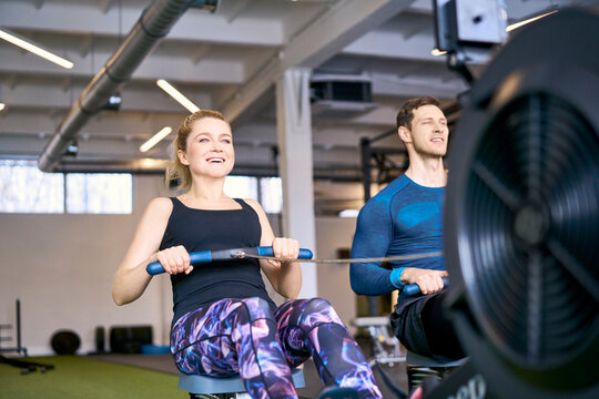 Man and woman at gym exercising together on rowing machines