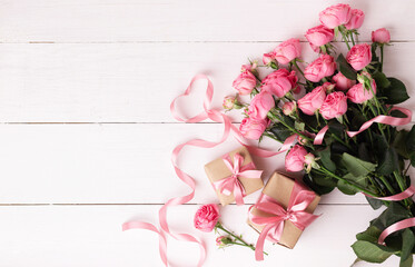 Fresh pastel soft pink roses, and gift boxes wrapped in kraft papper with ribbons on white wooden table.