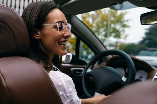 Smiling young woman driving convertible car in city