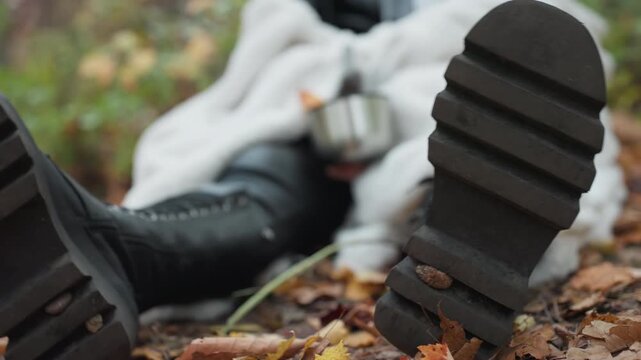 closeup heavy boot sole pressed into damp leaf litter, survivalist woman pauses holding steel cup, mud in tread and rugged texture dominate scene, gritty resilience and earthy fall palette