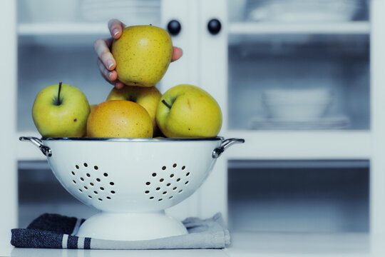 Close-up of a stack of apples in a colander on a kitchen worktop with a child's hand taking one