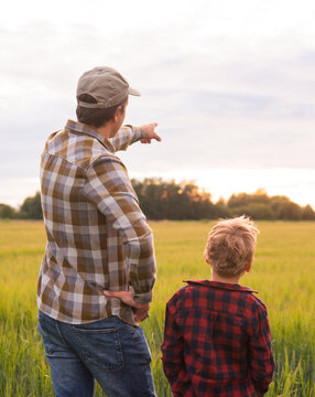 Farmer and his son in front of a sunset agricultural landscape. Man and a boy in a countryside field. Fatherhood, country life, farming and country lifestyle concept.