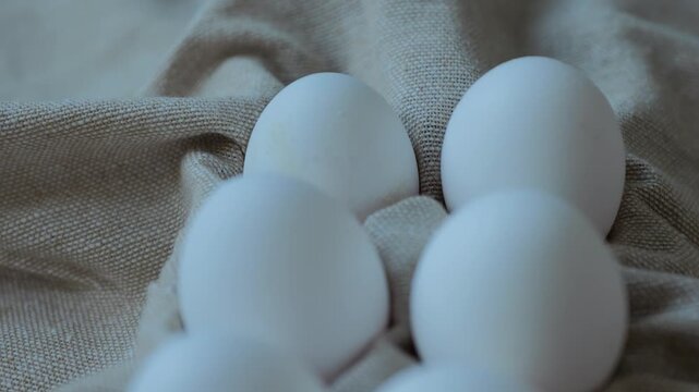 Six white eggs placed on a light cloth create a simple display in a kitchen. The setting is bright and clean.
