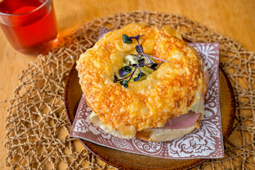Bagel with ham, cheese and salad leaf on plate, glass of fruity tea.
