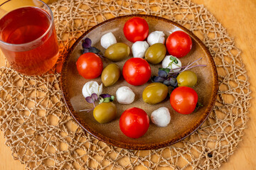 Plate with cherry tomato, mini mozarella and olive, glass of fruit tea.