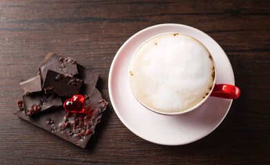 A cup of delicious, aromatic coffee with chocolate pieces and a red heart on a dark background