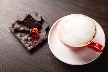 A cup of delicious, aromatic coffee with chocolate pieces and a red heart on a dark background