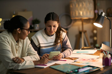 Naklejka premium Teenage Caucasian girl sitting at desk studying with middle aged Black woman tutor, both focusing on digital tablet surrounded by notebooks and educational materials during lesson