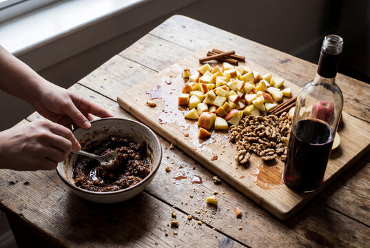 Hands of woman mixing traditional charoset with apple and walnut and cinnamon on rustic wooden table for Jewish Passover Seder meal preparation
