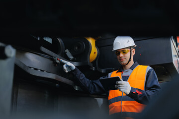 Male engineer using AI computer tablet for industrial machine inspection, control hydraulic system of excavator machinery