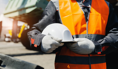 Male worker holding helmet at mining site with heavy machinery in background, banner