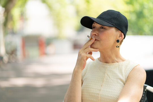 Mature woman smoking cigarette outdoors wearing a cap