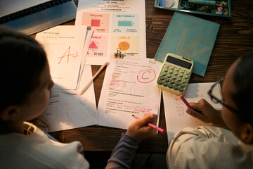 Two teenage girls, one Black and one Caucasian, studying together at desk, reviewing graded math...
